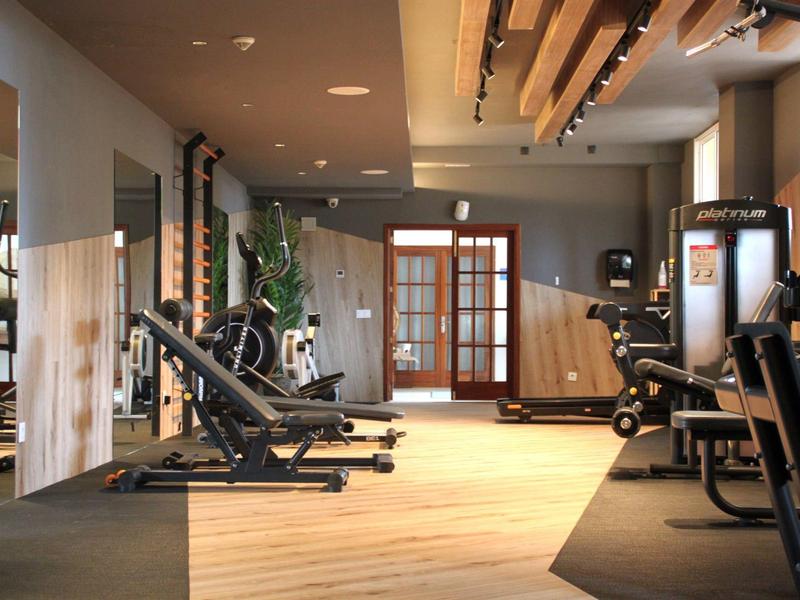 Dobrze oświetlona siłownia hotelowa z nowoczesnymi maszynami i drewnianą podłogą