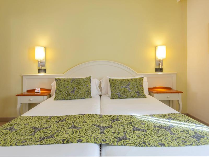 Przytulne dwa pojedyncze łóżka z zielonymi poduszkami i narzutami w ciepłym pokoju.