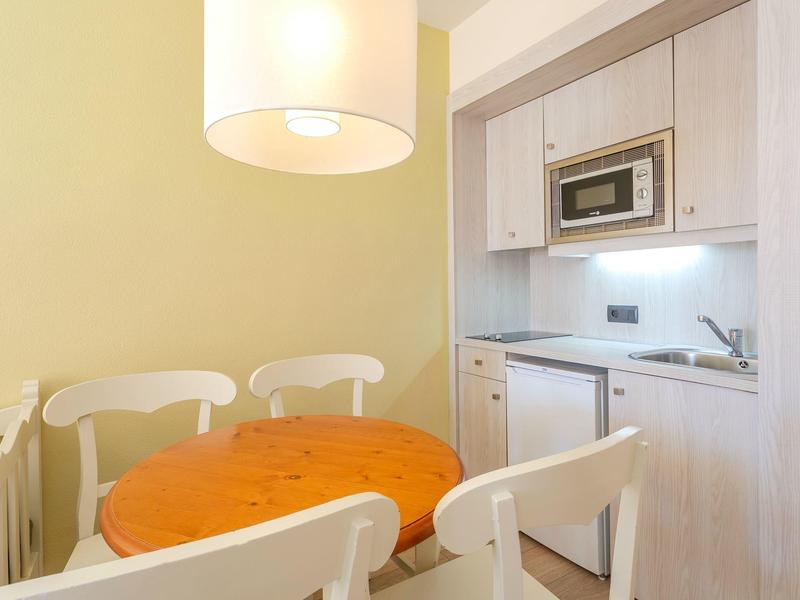 Przytulna jadalnia z okrągłym drewnianym stołem i białymi krzesłami obok kompaktowego aneksu kuchennego.