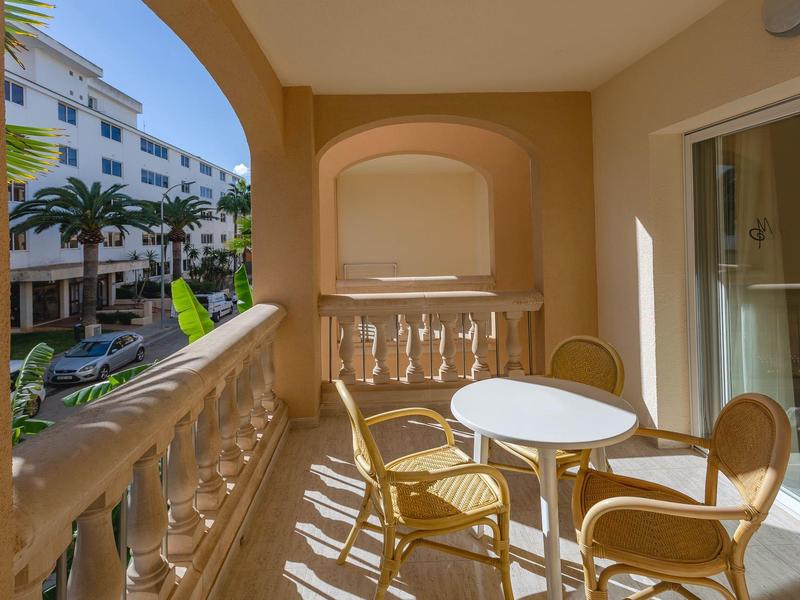 Słoneczny balkon z stołem i krzesłami z widokiem na ulicę z palmami i budynkami.