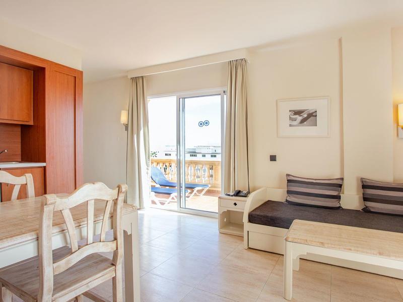 Jasny pokój hotelowy z aneksem kuchennym, jadalnią i balkonem z meblami na zewnątrz.