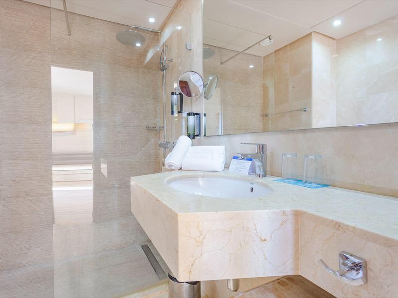 Nowoczesna łazienka hotelowa z marmurowymi ścianami i blatem, jasnym oświetleniem i dużym lustrem.