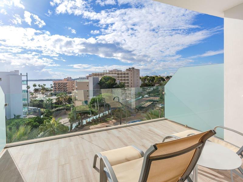 Balkon z krzesłami z widokiem na teren hotelu, basen i budynki pod częściowo pochmurnym niebem.