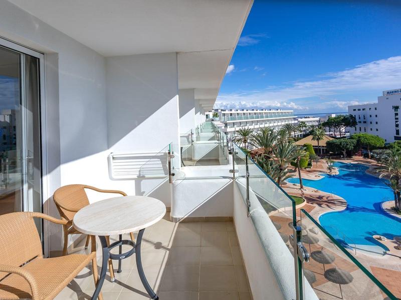 Balkon z stołem i krzesłami z widokiem na basen i hotele w słoneczny dzień.