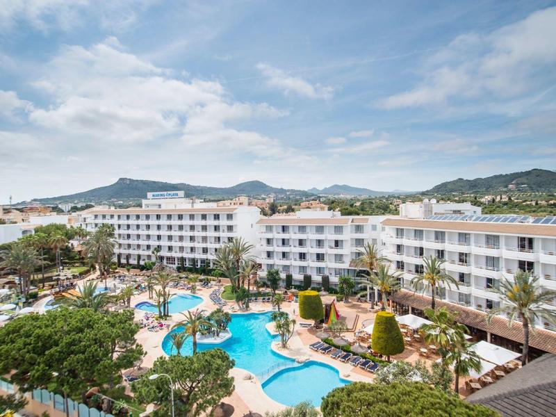 Kurort z dużym basenem, otoczony drzewami i białymi wielopiętrowymi budynkami pod niebieskim niebem.