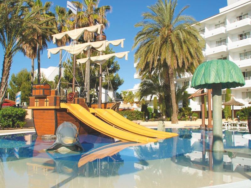 Kolorowy plac zabaw wodnych ze zjeżdżalniami i palmami przy budynku hotelu.