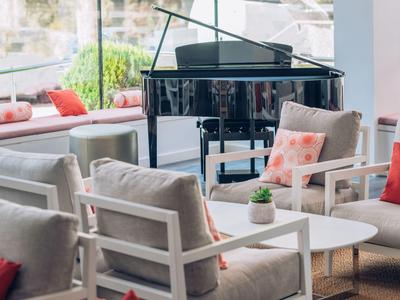 Moderne Lounge mit grauen Sesseln, weißen Tischen, bunten Kissen und schwarzem Flügelklavier.