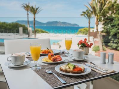 Tavolo per la colazione con succo, caffè e croissant con vista su palme e mare.