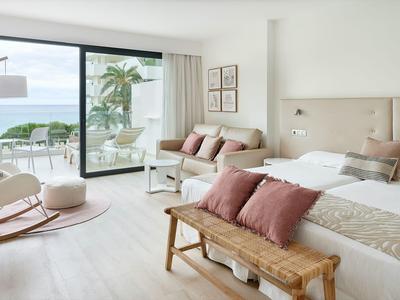 Camera d'hotel luminosa con letto grande, divano, panche di legno e vista sul mare attraverso grandi finestre.