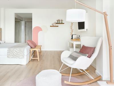 Luminoso camera d'hotel con letto matrimoniale, sedia a dondolo, sgabello e illuminazione moderna.