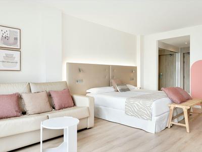 Camera d'albergo luminosa con letto, divano, cuscini e pavimento in legno minimalista.