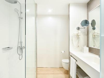 Bagno moderno e luminoso con doccia, WC e grande specchio con lavabo.