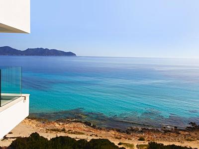 Uitzicht vanaf een hotelbalkon op de rustige turquoise zee en rotsachtig strand.