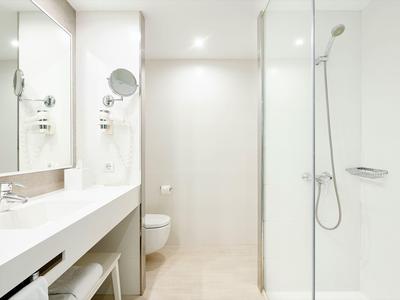 Lichte, moderne badkamer met grote douche, toilet en lange wastafel met spiegel.