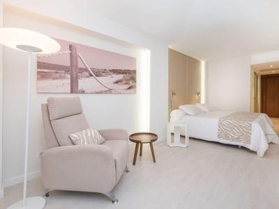 Helles, modernes Schlafzimmer mit weißem Sessel, Stehlampe, Holz-Nachttisch und großem Bett.