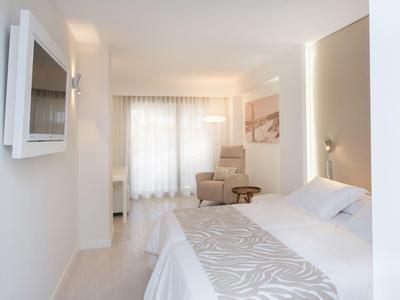 Helles, modernes Schlafzimmer mit großem Bett, weißen Wänden und einem Sessel am Fenster.