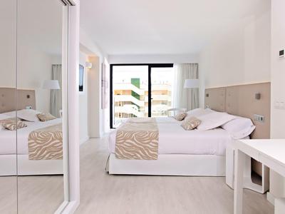 Helles Schlafzimmer mit großem Bett, beiger Bettwäsche, Spiegeln und Balkon mit Glasgeländer.