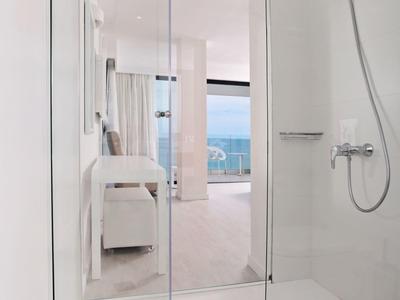 Moderne, helle Dusche mit Glaswand, weißem Duschboden und Handbrause, Blick ins Schlafzimmer.