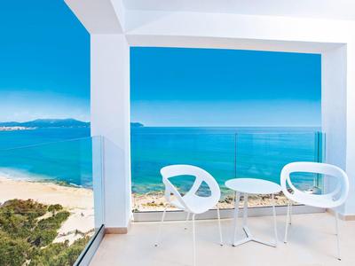Balkon mit weißen Stühlen und Tisch, Blick auf Strand, Meer und blauen Himmel.