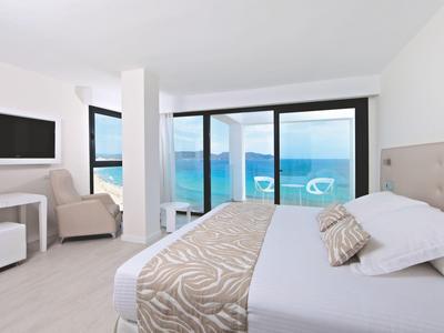 Camera d'hotel moderna con letto matrimoniale, zona soggiorno e vista mare tramite grandi finestre.