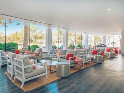 Großer heller Raum mit weißen Sitzmöbeln, roten Kissen, Glaswänden und Holzboden.