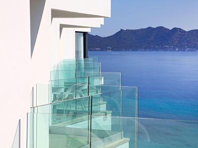 Balconi con ringhiere in vetro su edificio bianco con vista sul mare blu e montagne.