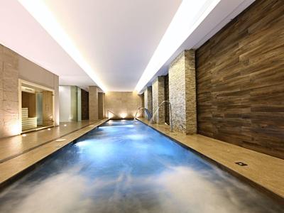 Modernes Hallenbad mit langem Wasserbecken, warmem Licht, Holz- und Steinverkleidung.