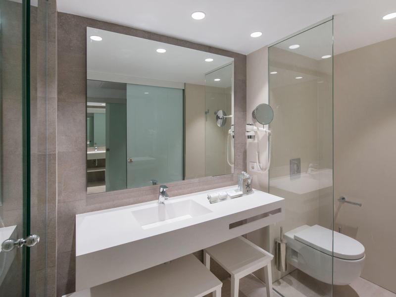 Modernes Badezimmer mit Glasdusche, weißem Waschbecken, Spiegeln und gedeckten Wandfarben.