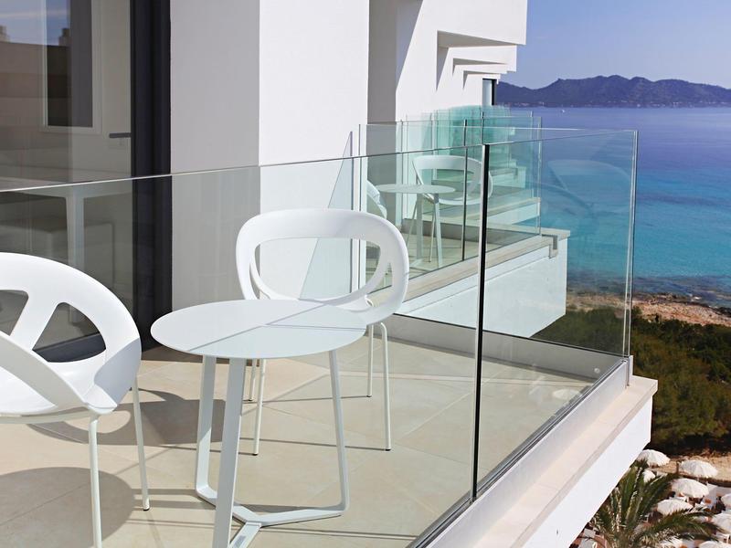 Moderner Balkon mit weißen Stühlen und Glaskante, Blick auf blauen Ozean und Berge im Hintergrund.