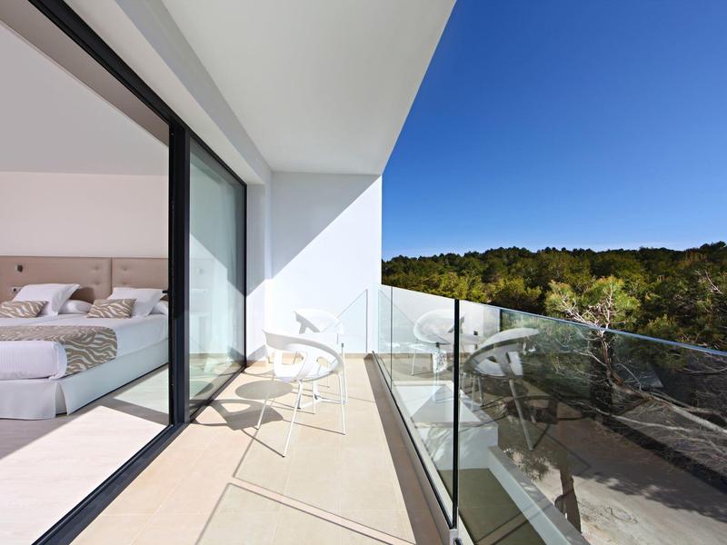 Moderner Balkon mit Glasgeländer, weißen Stühlen, Blick auf grüne Bäume und blauen Himmel.