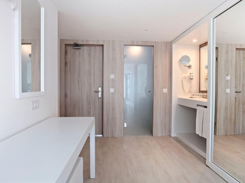 Heller Flur mit Holztür, großem Spiegel, weißem Tisch und grauem Bodenbelag.