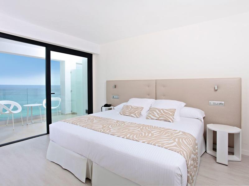 Helles Schlafzimmer mit großem Doppelbett, beigem Kopfteil und bodentiefen Fenstern zum Meer.