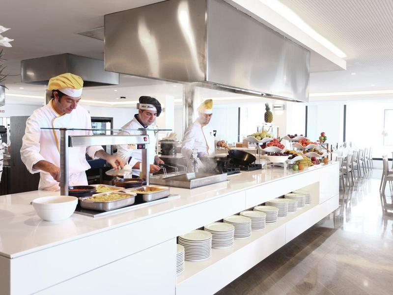 Moderne Cafeteria mit mehreren Köchen, hellen Farben und großem, offenem Kochbereich.