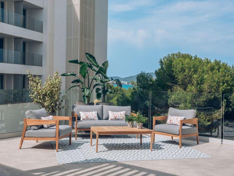 Moderner Balkon mit grauen Polstersesseln und Sofa, Holztisch, Teppich und grünen Pflanzen.