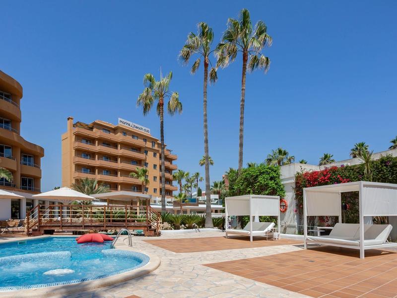 Area piscina moderna con lettini, palme e hotel su più piani sotto un cielo sereno.