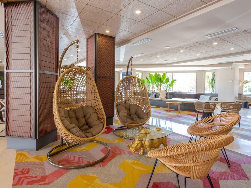 Zona lounge dell'hotel luminosa con sedie in rattan moderne e tappeto colorato.