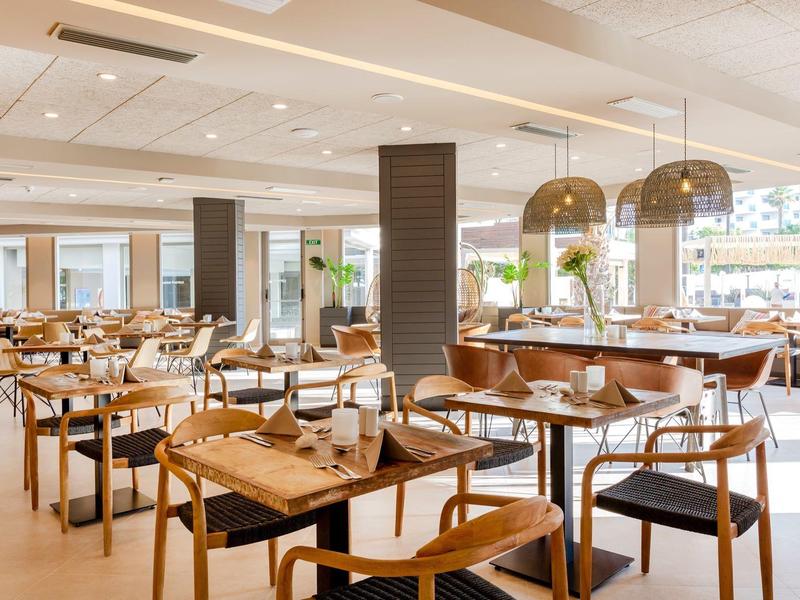 Ristorante luminoso e moderno con tavoli e sedie in legno e grandi finestre che lasciano entrare molta luce.