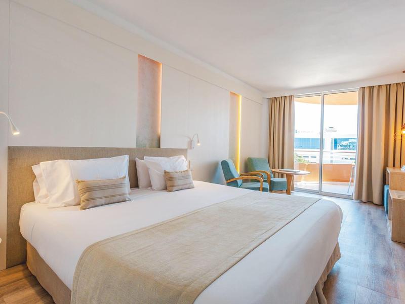 Camera d'hotel moderna con letto matrimoniale, zona salotto e balcone con vista mare.