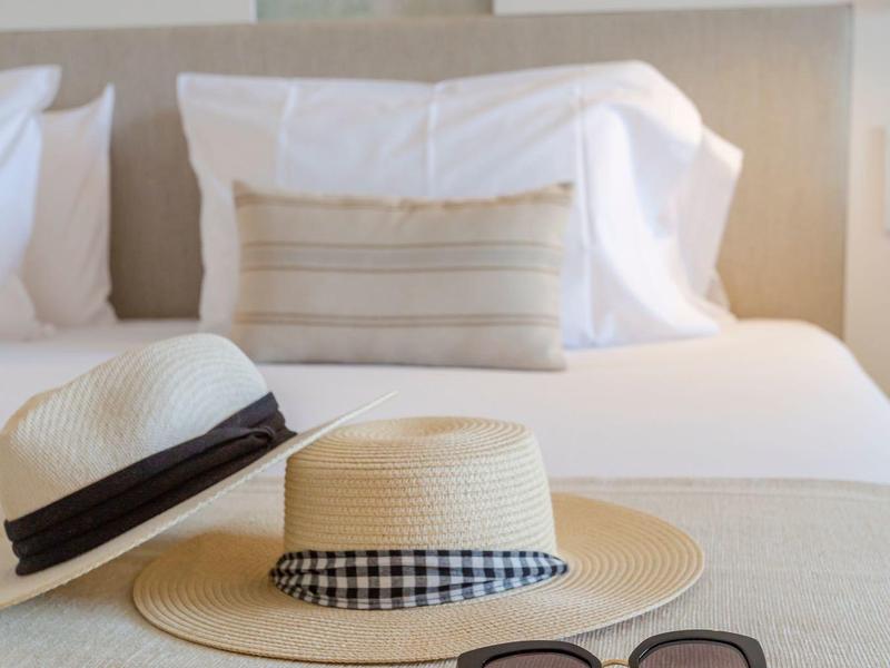 Un cappello di paglia e degli occhiali da sole sono posati su un letto in una camera d'hotel moderna.