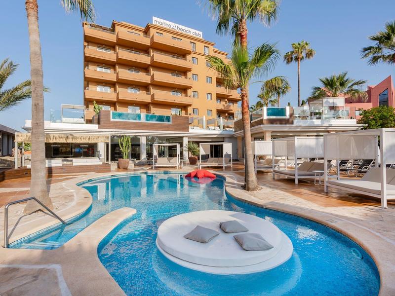 Hotel con piscina all'aperto, lettini e palme, edificio moderno su più piani sullo sfondo.