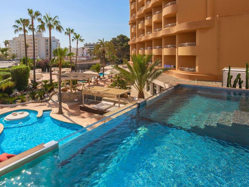 Piscina a sfioro con vista su giardino e palme accanto all'hotel in ambiente soleggiato.
