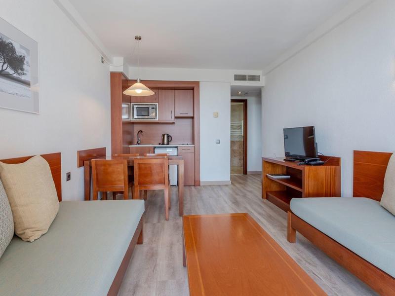 Soggiorno luminoso con due divani, tavolo da pranzo e cucina aperta in una stanza d'hotel.