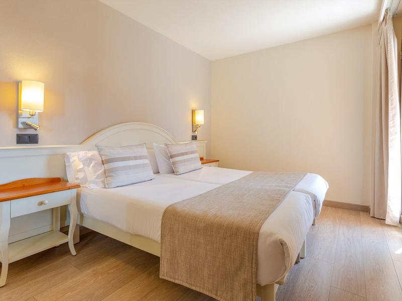 Camera d'hotel luminosa con grande letto matrimoniale, due comodini e lampade da parete calde.