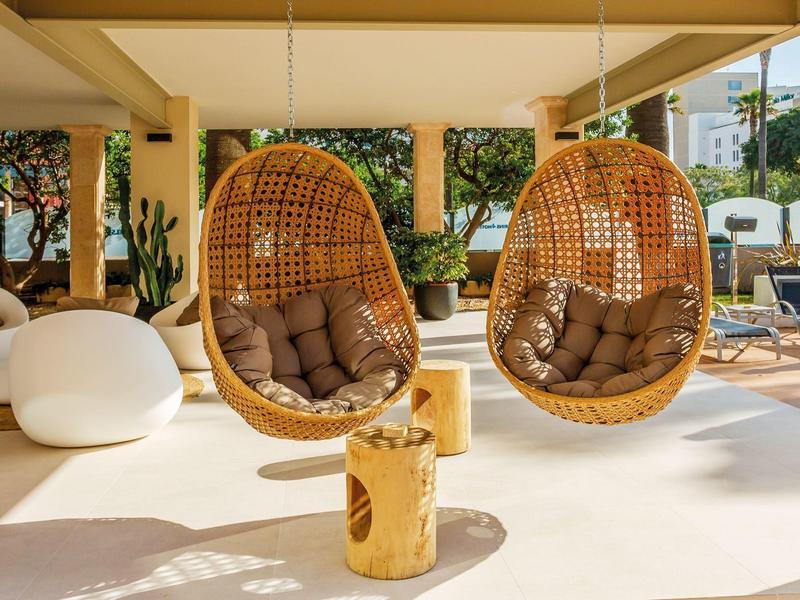 Terrazza luminosa con due sedie sospese in vimini e cuscini accoglienti.