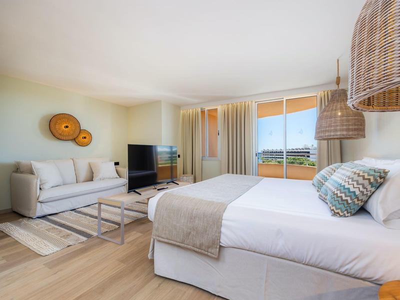 Camera luminosa con letto matrimoniale, divano, TV a schermo piatto e balcone con vista mare.