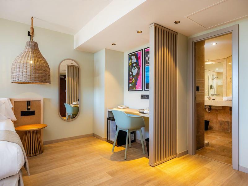 Camera d'hotel moderna con scrivania, sedia, specchio e bagno separato