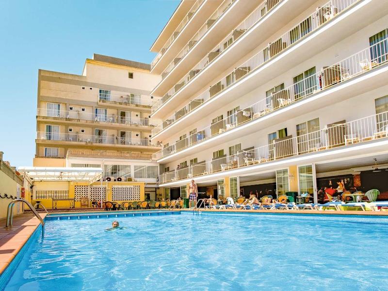 Large outdoor pool in front of a multi-story hotel building with sun loungers.