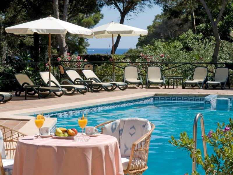 Area piscina con lettini e un tavolo con bevande e frutta in un ambiente tropicale.