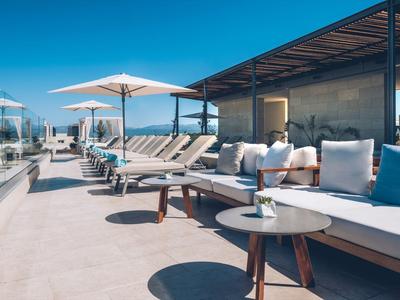 Luxury poolside lounge area with sunbeds, umbrellas, and modern seating under a clear sky.