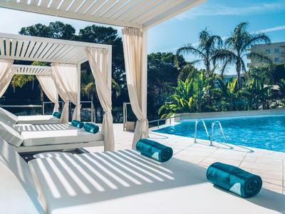 Moderner Poolbereich mit weißen Liegen, blauen Handtüchern und Palmen im Hintergrund.